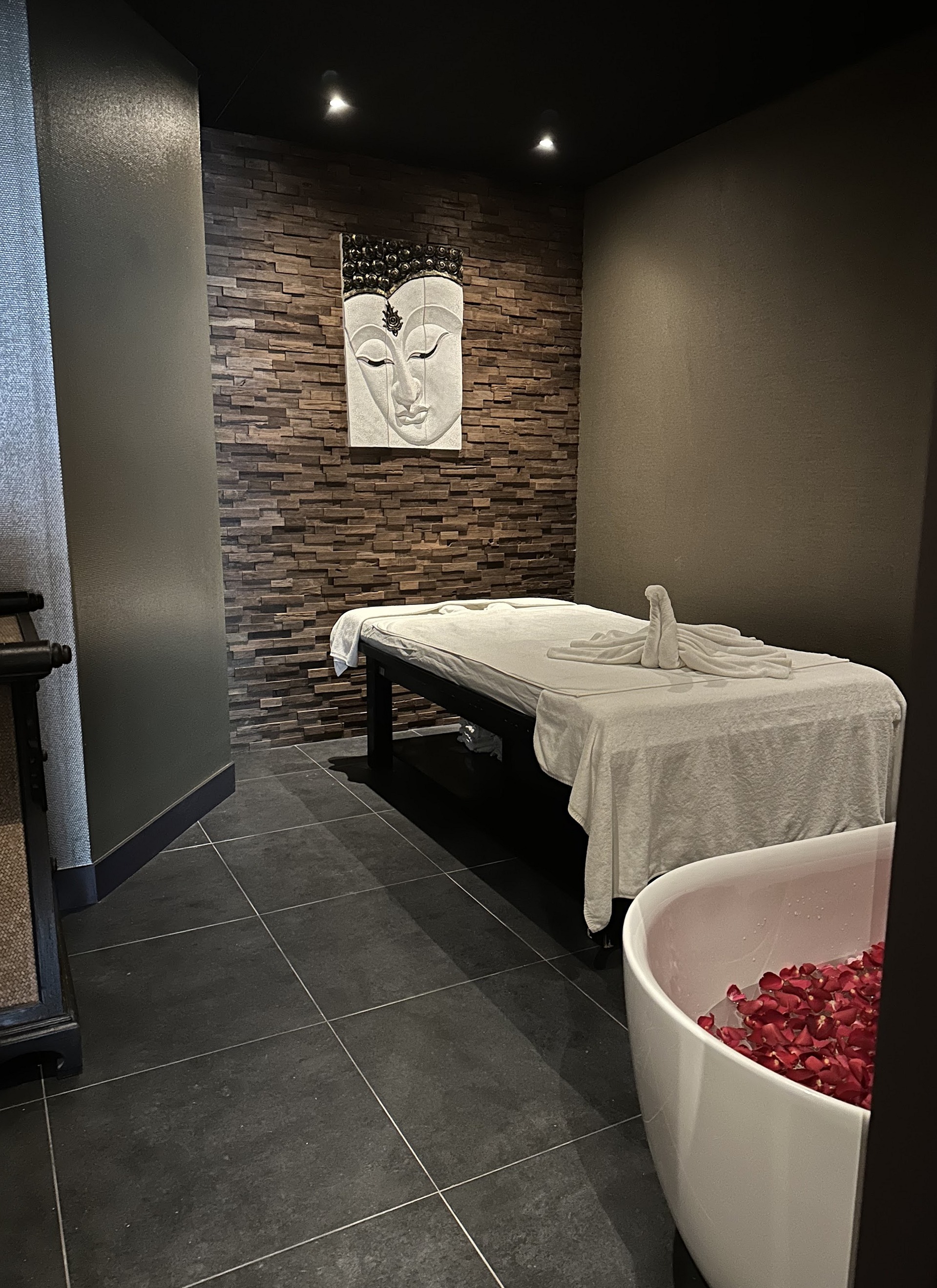 Massagekamer met wit opgemaakt massagebed en bad met rozenblaadjes